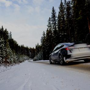 E-Auto fährt auf Strasse durch verschneiten Wald